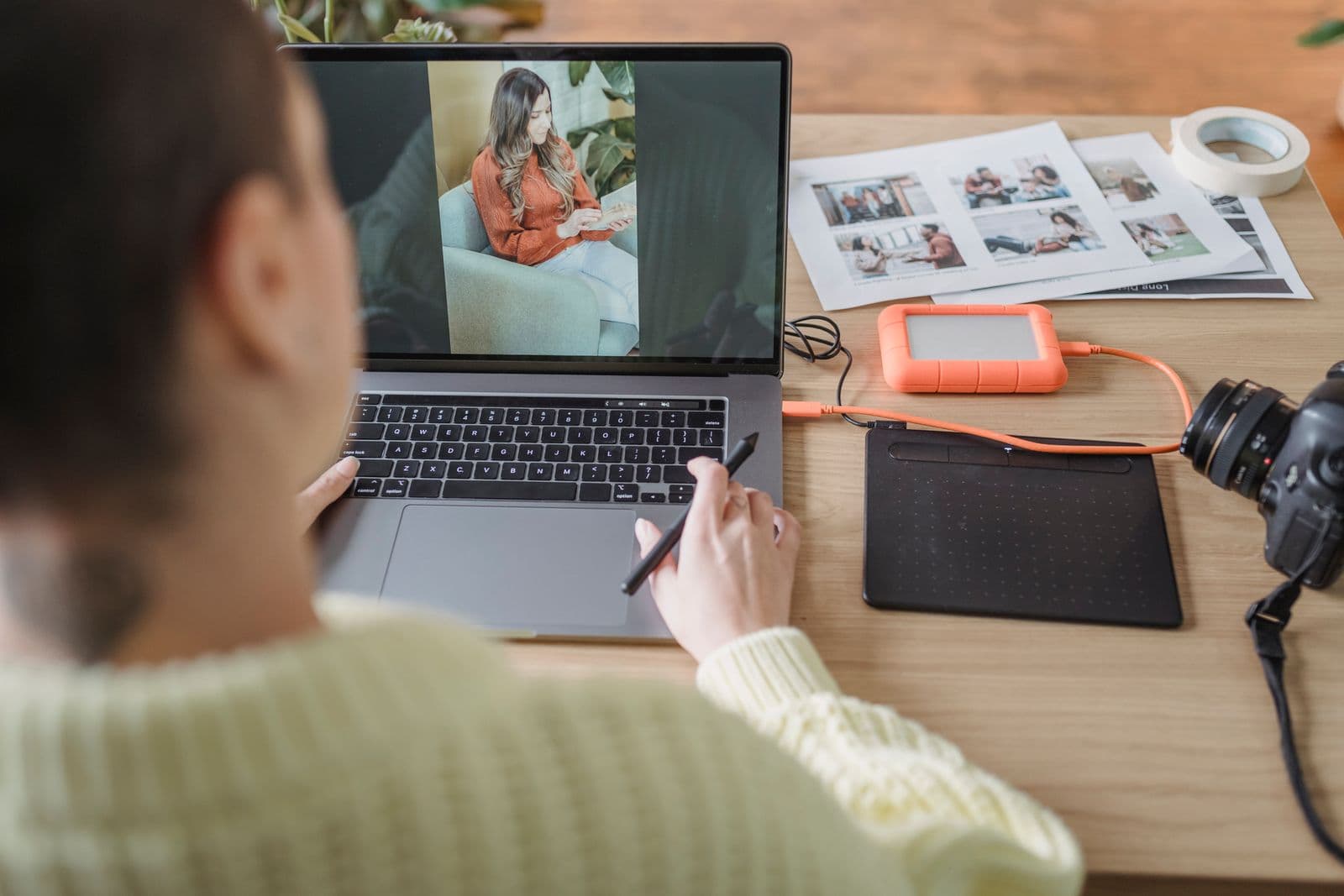 Photographer working beside a laptop, camera, prints, and external drive