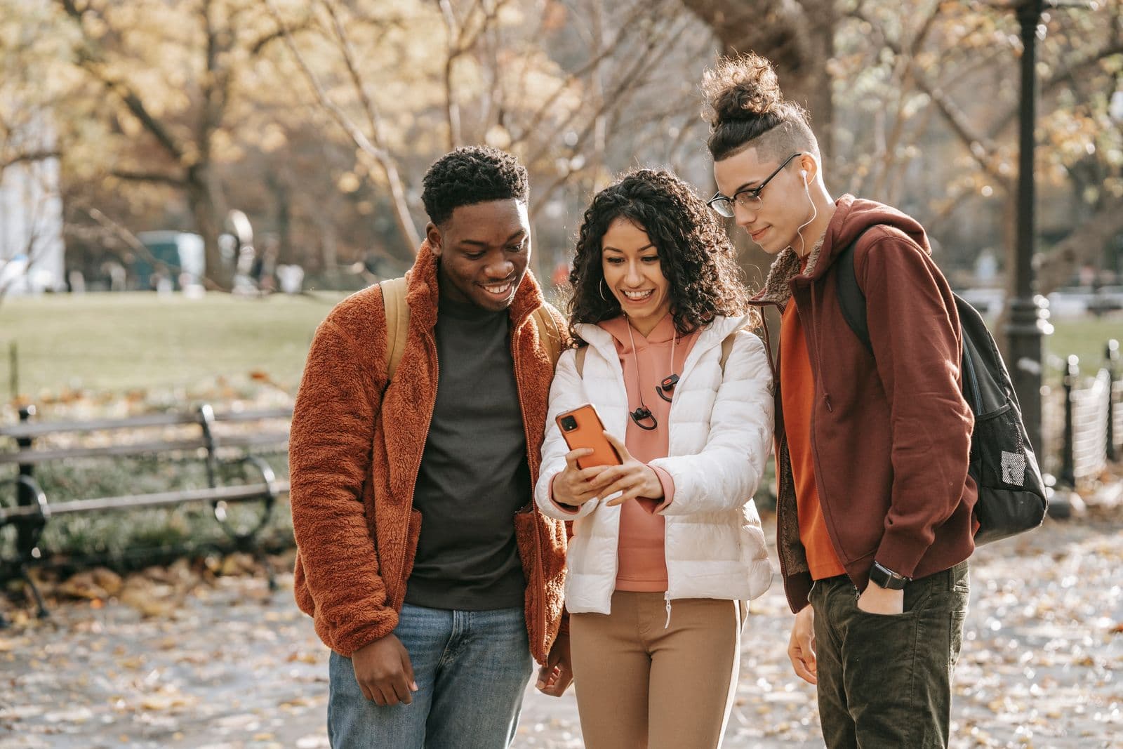 Freunde in einem herbstlichen Park schauen gemeinsam auf ein Smartphone
