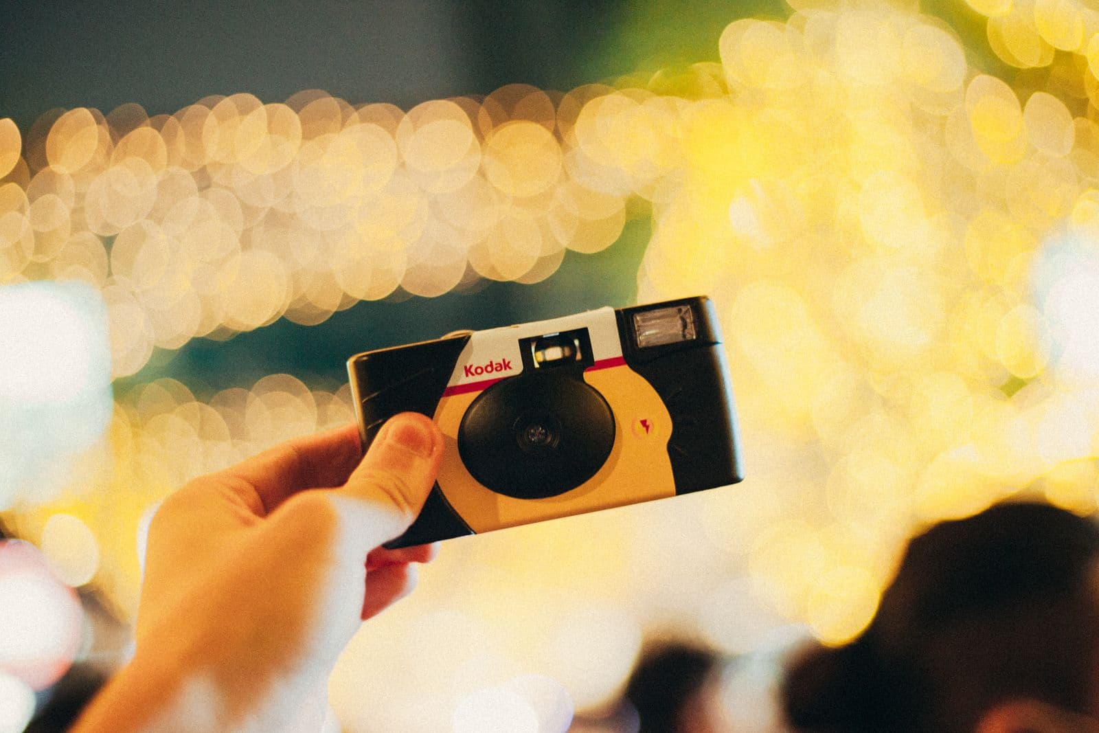 Hand holding a disposable film camera against colourful party lights