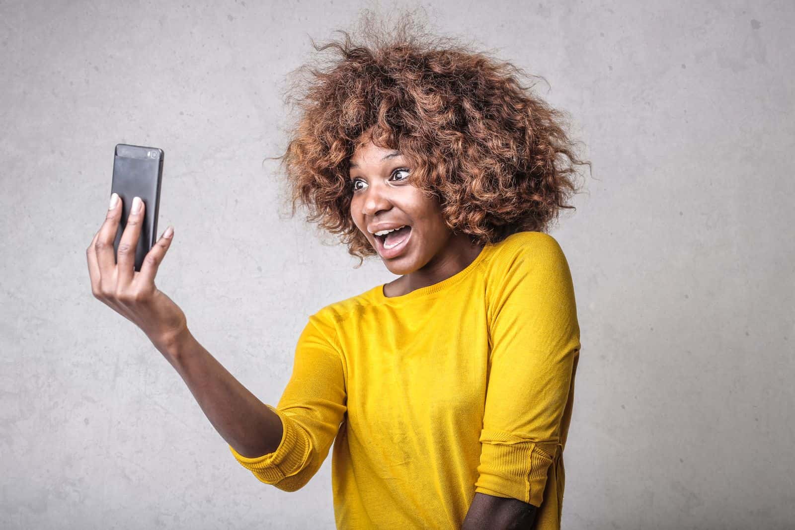 Woman smiling while taking a selfie with her phone indoors