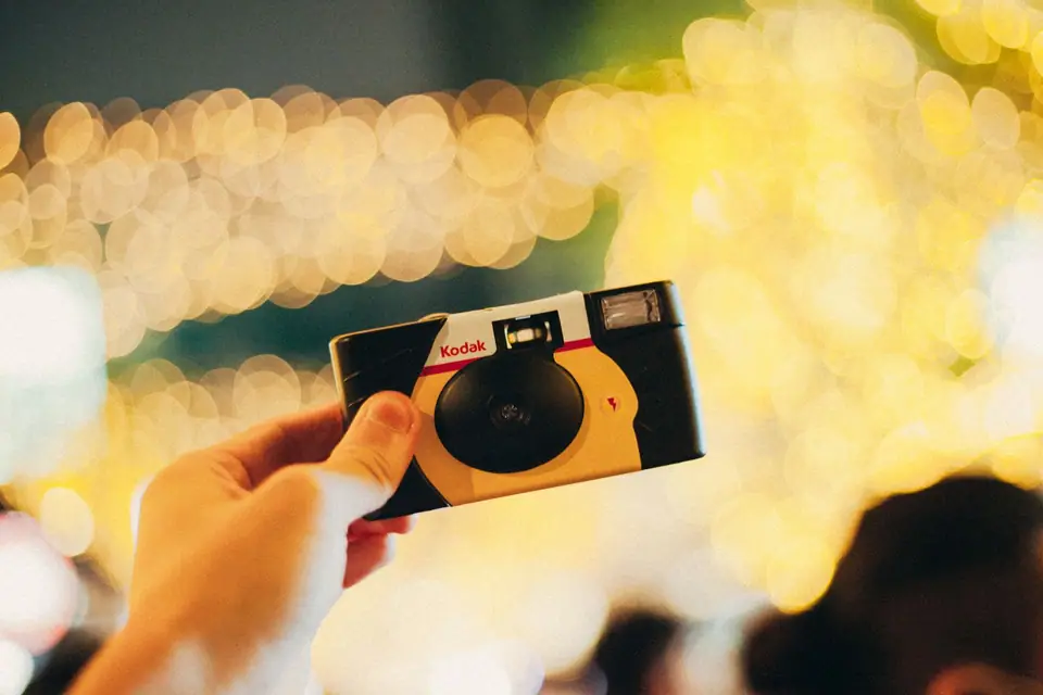 Hand holding a disposable film camera against colourful party lights